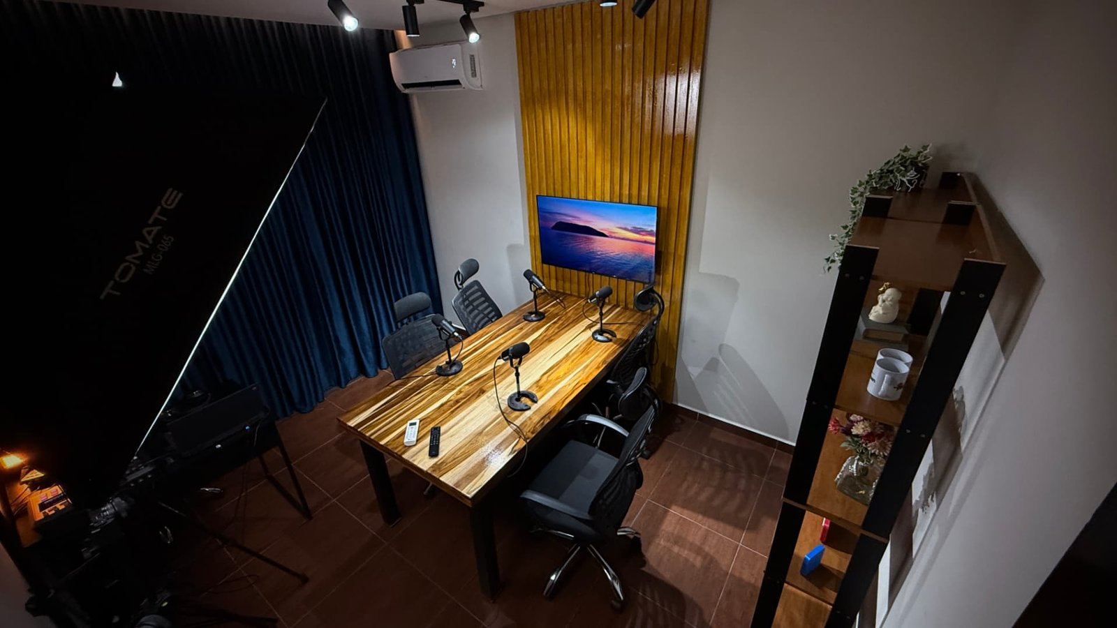 Vista ampla do estúdio com mesa de gravação, microfones e painel de madeira